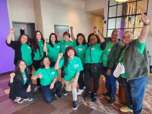 Eleven of UDW's members wearing their UDW shirts raise their fists and pose for a photo.